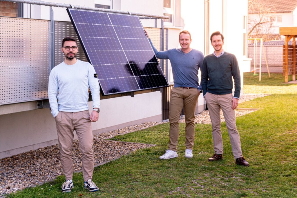 Drei Männer neben einem Photovoltaik-Modul, das an einem Balkon befestigt ist.